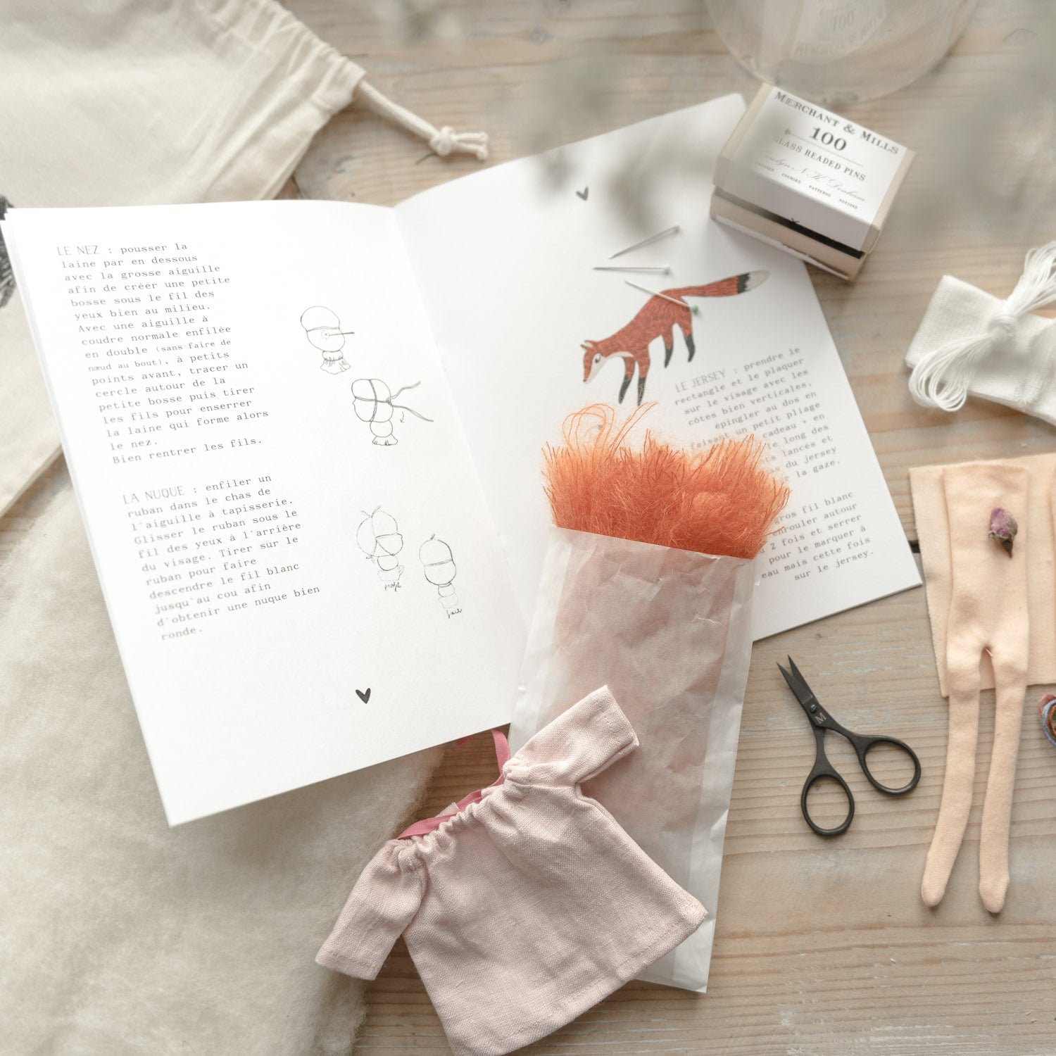 Doll kit pieces, sewing tools, thread, and booklet arranged on a wooden table